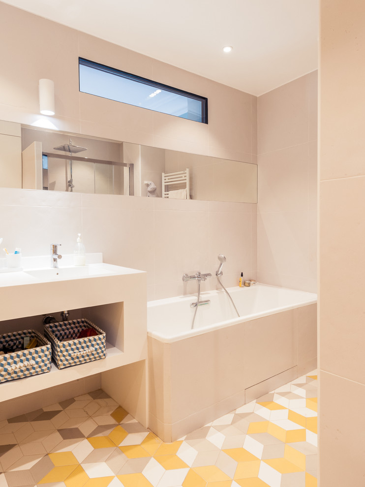 Photo of a retro ensuite bathroom in Paris with an integrated sink, a submerged bath, a built-in shower, a wall mounted toilet, yellow tiles, ceramic tiles, grey walls and ceramic flooring.