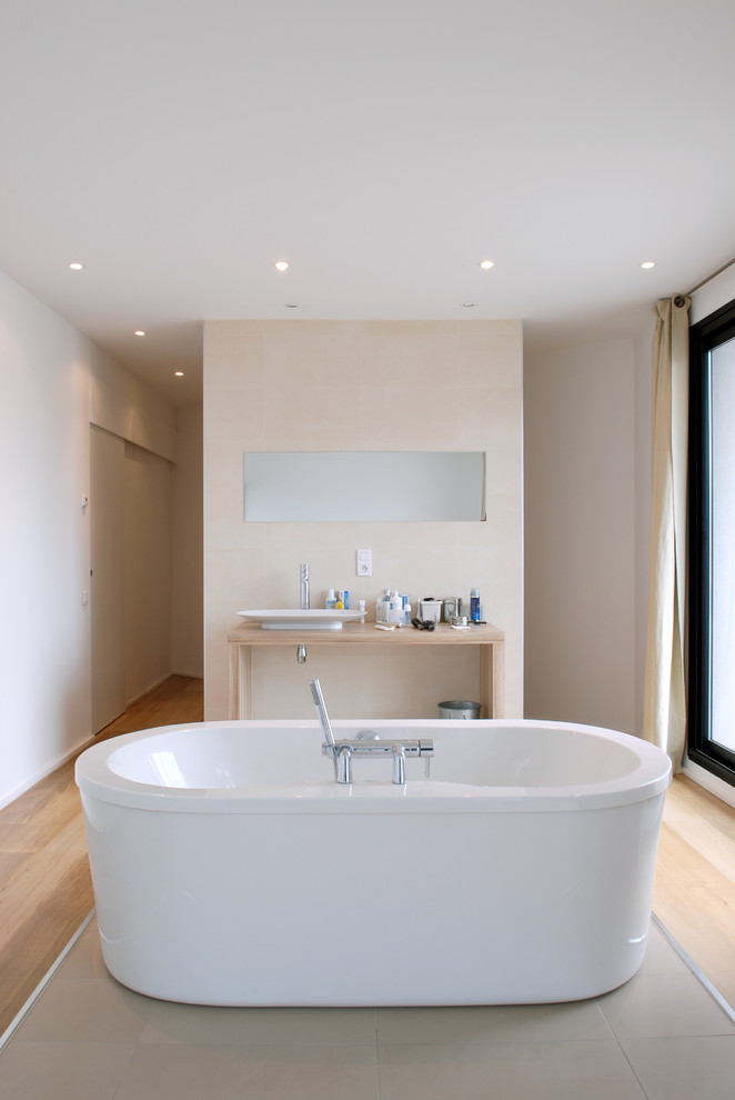 Inredning av ett modernt mellanstort beige beige en-suite badrum, med ett fristående handfat, ett fristående badkar, beige väggar, ljust trägolv och träbänkskiva