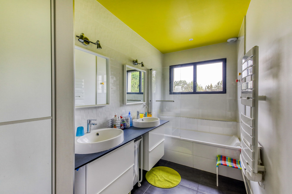 Idées déco pour une salle de bain grise et jaune contemporaine avec un placard à porte plane, des portes de placard blanches, une baignoire en alcôve, un carrelage gris, une vasque, un sol noir et un plan de toilette noir.