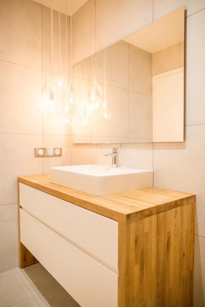 На фото: ванная комната среднего размера в скандинавском стиле с плоскими фасадами, белыми фасадами, бежевой плиткой, бежевыми стенами, накладной раковиной, столешницей из дерева, бежевым полом и коричневой столешницей с