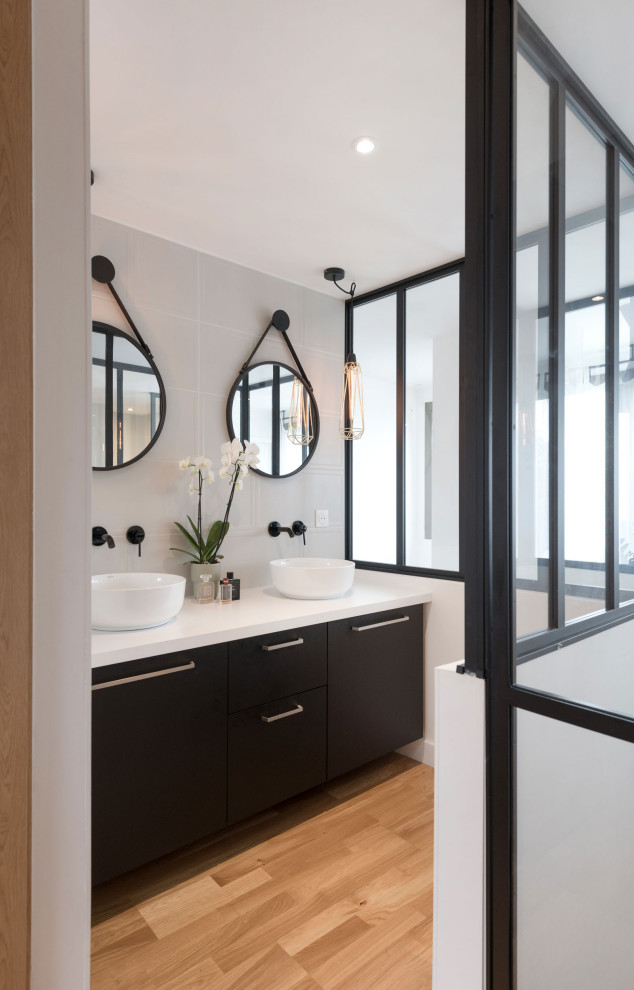 Bathroom - mid-sized contemporary master ceramic tile and gray tile medium tone wood floor and brown floor bathroom idea in Lyon with black cabinets, solid surface countertops, white countertops, white walls, flat-panel cabinets and a vessel sink