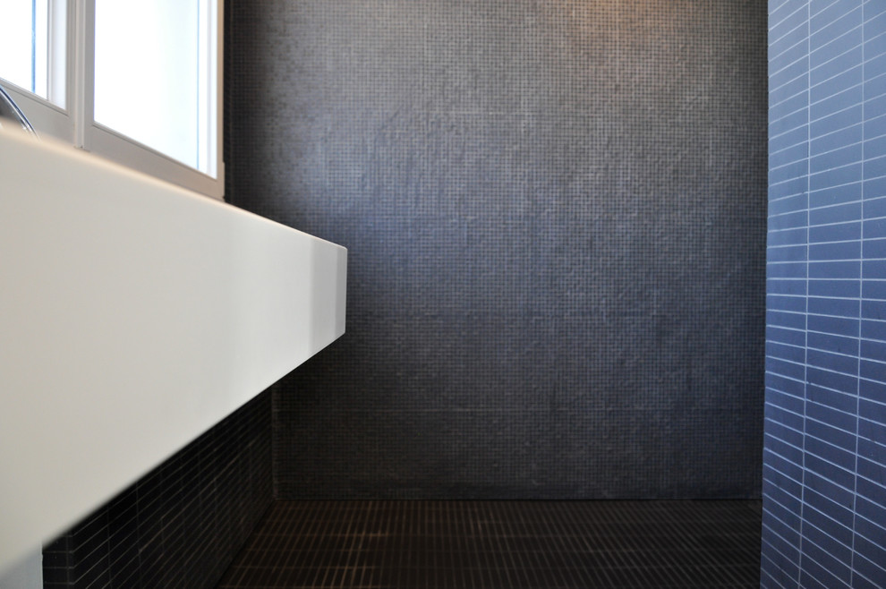 Réalisation d'une petite salle d'eau design avec des portes de placard grises, une douche ouverte, un carrelage gris, un mur blanc, une grande vasque, un plan de toilette en surface solide et un sol en carrelage de céramique.