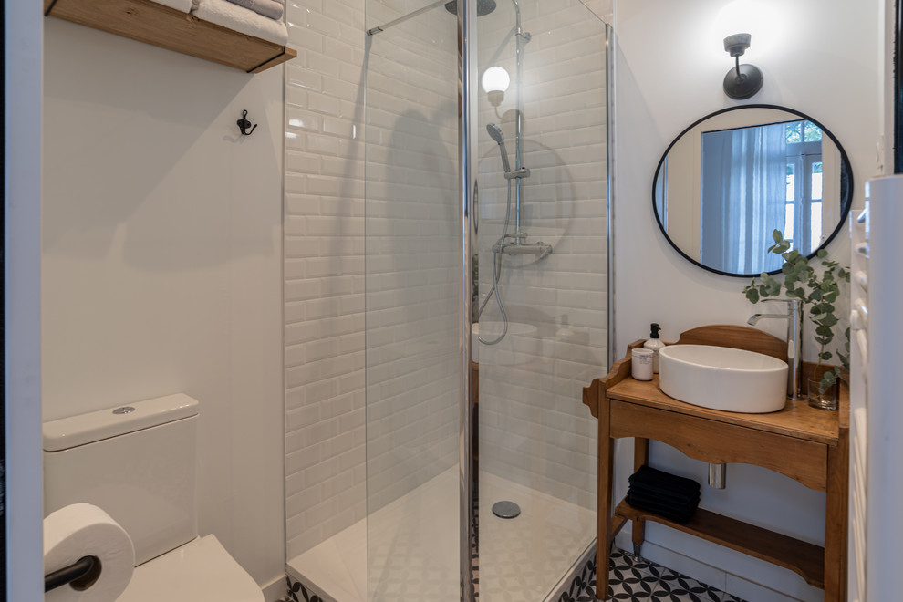 Inspiration for a mid-sized eclectic 3/4 white tile and subway tile cement tile floor and black floor corner shower remodel in Nice with open cabinets, a one-piece toilet, white walls, a drop-in sink, wood countertops, a hinged shower door and brown countertops
