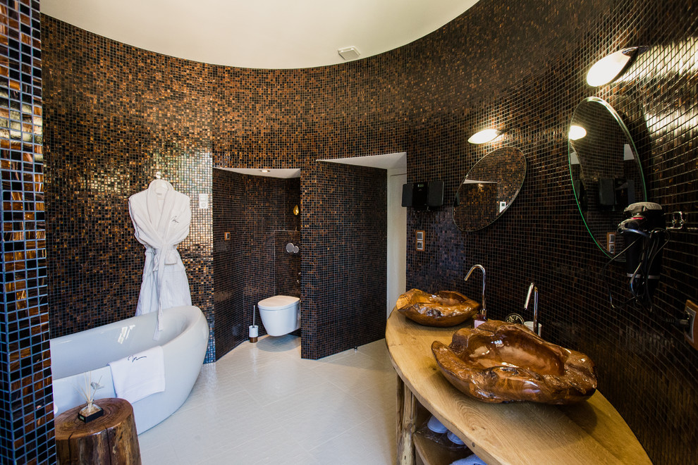 Modern inredning av ett stort en-suite badrum, med ett fristående badkar, en vägghängd toalettstol, flerfärgad kakel, mosaik, ett fristående handfat, träbänkskiva, flerfärgade väggar och en dusch i en alkov
