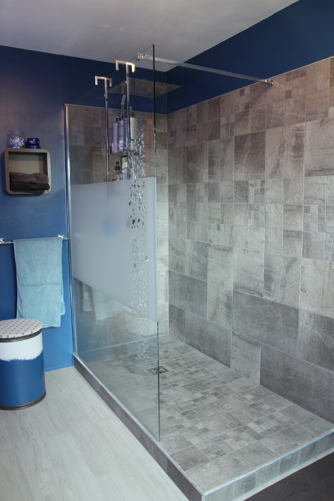 Bild på ett mellanstort funkis badrum, med bruna skåp, ett hörnbadkar, en öppen dusch, grå kakel, stenkakel, blå väggar, vinylgolv, ett avlångt handfat, grått golv och med dusch som är öppen