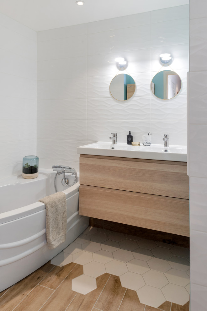 Cette image montre une salle de bain principale nordique en bois clair de taille moyenne avec un placard à porte affleurante, une baignoire d'angle, un carrelage blanc, des carreaux de céramique, un mur bleu, un lavabo suspendu, un sol blanc et un sol en carrelage de céramique.