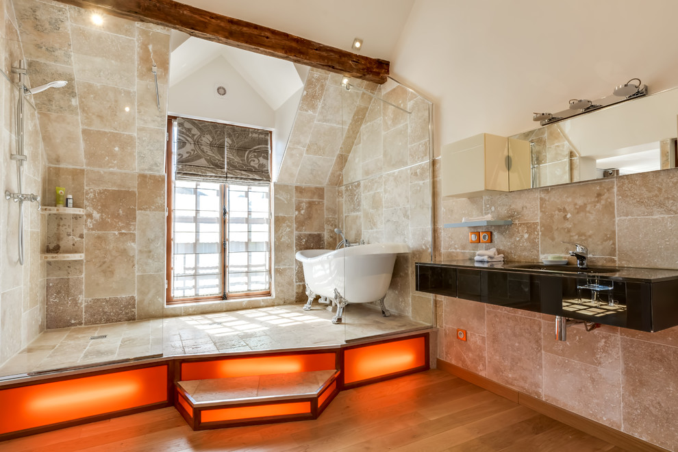 Cette image montre une grande douche en alcôve principale bohème avec une baignoire sur pieds, un carrelage beige, un mur beige, un sol en bois brun et un lavabo intégré.