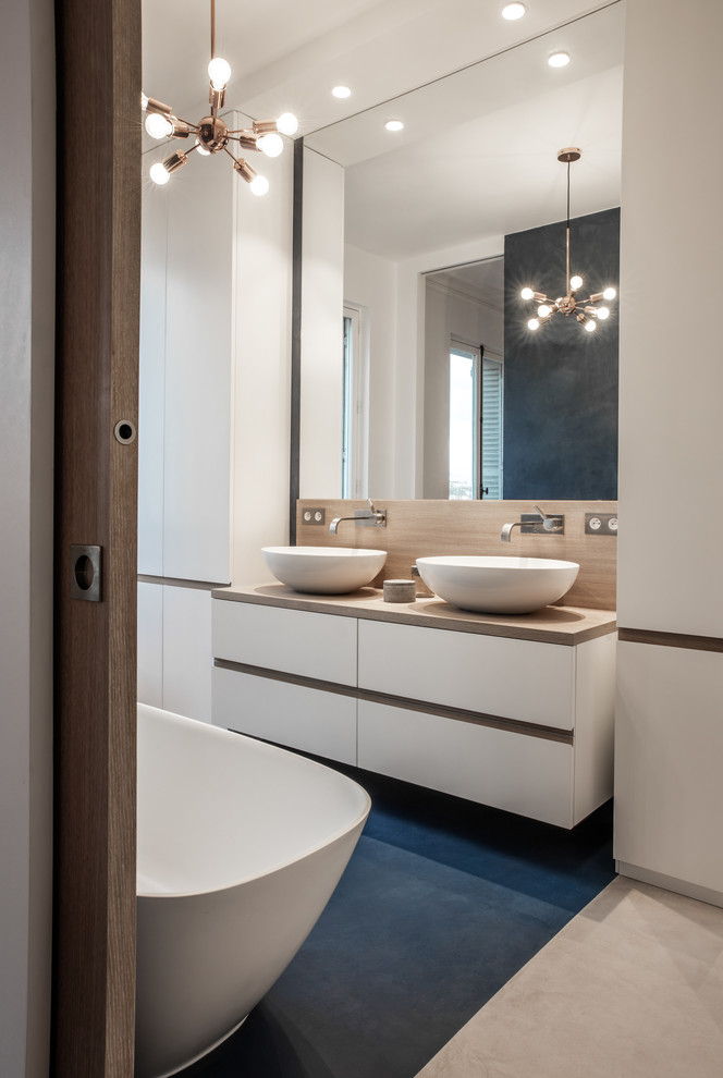 Inredning av ett modernt stort beige beige en-suite badrum, med vita skåp, ett fristående badkar, betonggolv, träbänkskiva, blått golv, släta luckor, vita väggar och ett fristående handfat