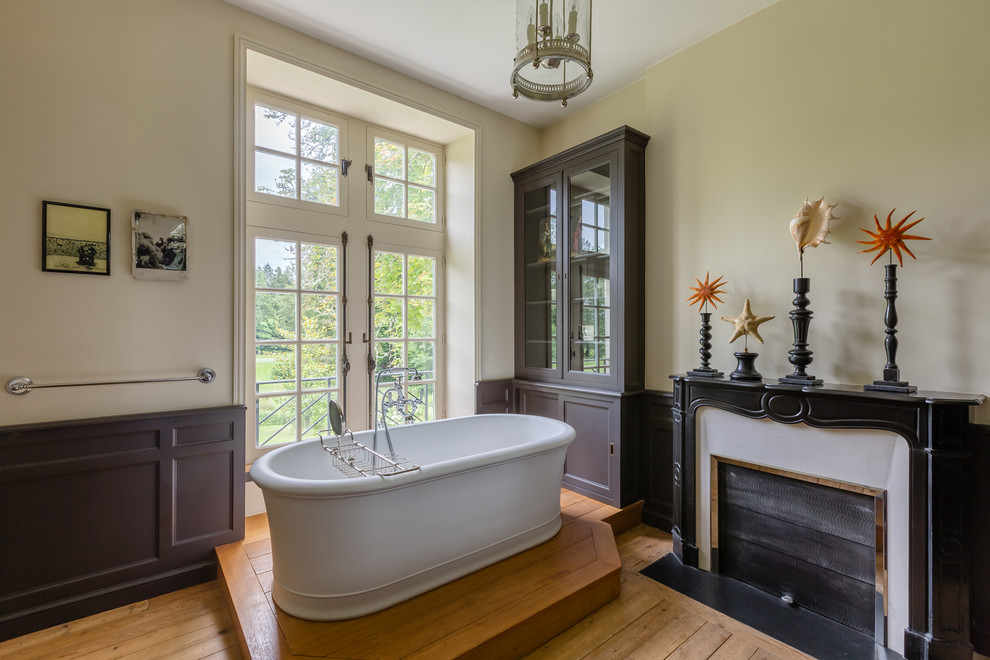 Cette image montre une salle de bain principale traditionnelle avec une baignoire indépendante, un mur beige et un sol en bois brun.