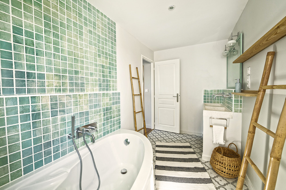 Réalisation d'une salle de bain principale méditerranéenne de taille moyenne avec une baignoire d'angle, WC suspendus, un carrelage vert, des carreaux en terre cuite, un mur gris, tomettes au sol, un plan vasque et un plan de toilette en terrazzo.