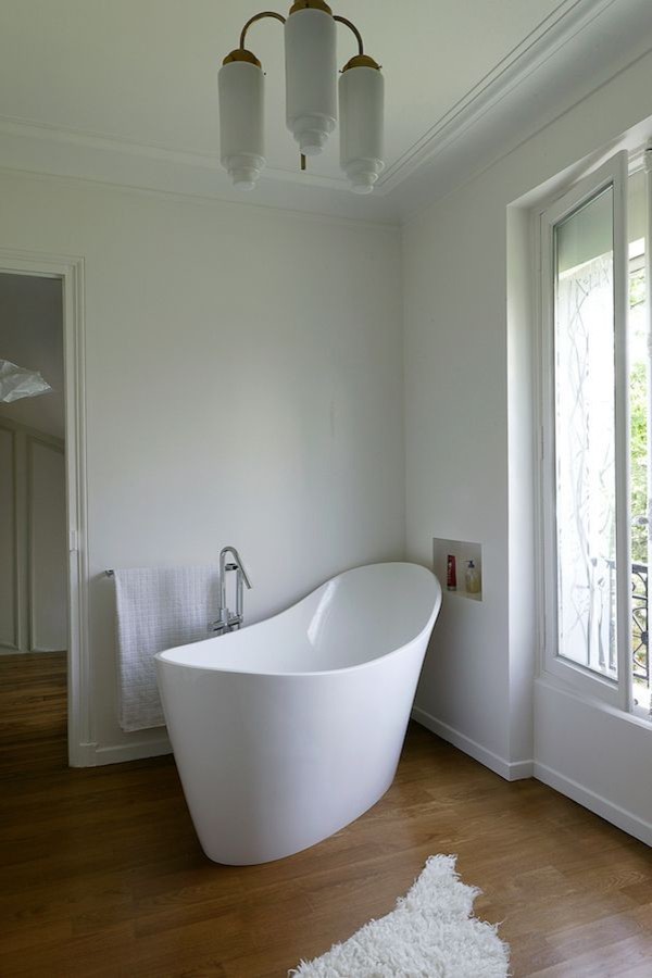 Cette image montre une salle de bain principale minimaliste de taille moyenne avec une baignoire indépendante, un mur blanc, un sol en bois brun et une fenêtre.