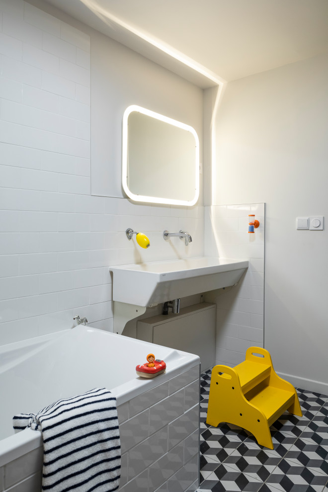 На фото: ванная комната в современном стиле с угловой ванной, белой плиткой, белыми стенами, подвесной раковиной, разноцветным полом и тумбой под одну раковину