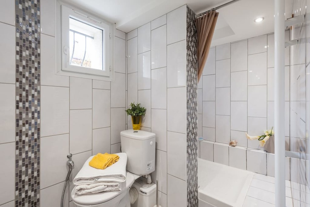 Inredning av ett modernt mellanstort badrum med dusch, med en öppen dusch, en toalettstol med hel cisternkåpa, vit kakel, keramikplattor, vita väggar, klinkergolv i keramik, ett avlångt handfat, laminatbänkskiva, vitt golv och med dusch som är öppen