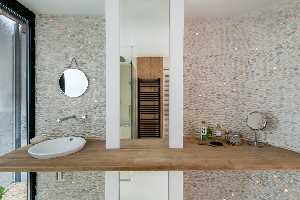 Esempio di una stanza da bagno con doccia stile marino di medie dimensioni con piastrelle beige, piastrelle di ciottoli, pareti bianche, lavabo sottopiano e top in legno