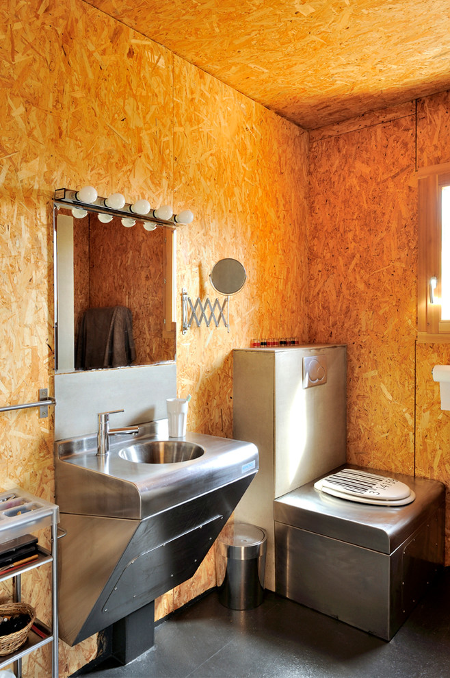Cette photo montre une salle de bain industrielle de taille moyenne avec un lavabo suspendu, un plan de toilette en acier inoxydable, un mur marron et WC à poser.