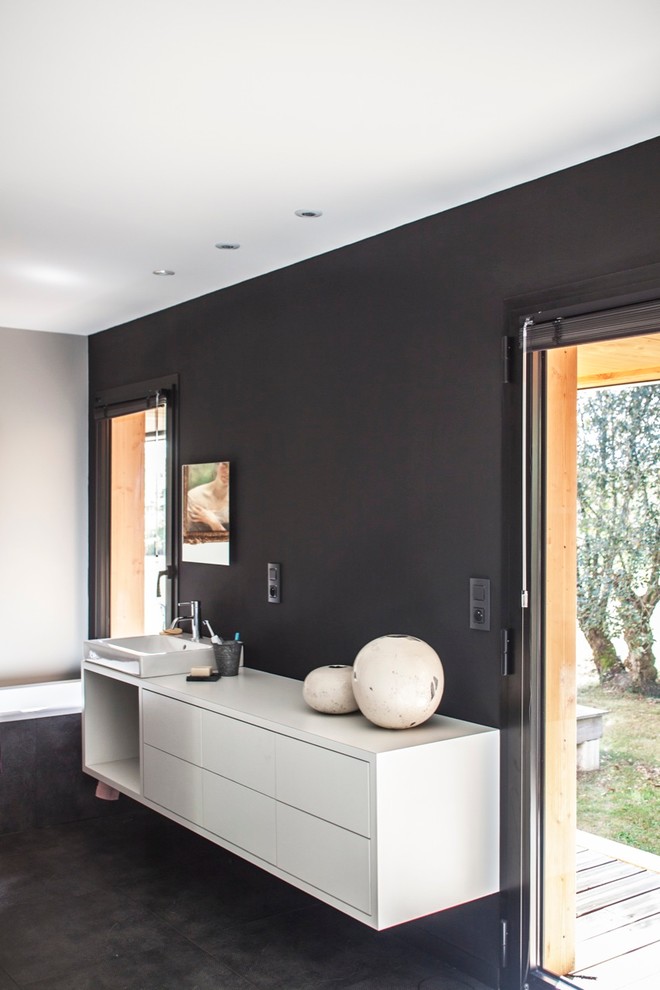 Cette image montre une grande salle de bain principale design avec des portes de placard blanches, un mur noir et une vasque.