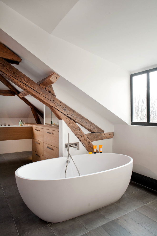 Trendy freestanding bathtub photo in Paris with flat-panel cabinets, medium tone wood cabinets and white walls