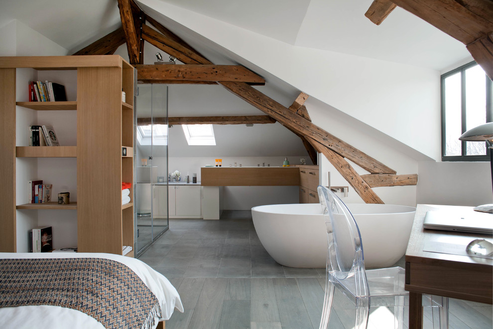 Modernes Duschbad mit Einbaubadewanne, flächenbündigen Schrankfronten, hellbraunen Holzschränken, weißer Wandfarbe, gebeiztem Holzboden, Waschtisch aus Holz, grauem Boden und freigelegten Dachbalken in Paris