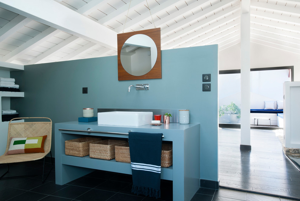 Diseño de cuarto de baño costero con armarios abiertos, puertas de armario azules, paredes azules, lavabo sobreencimera, suelo negro y encimeras azules