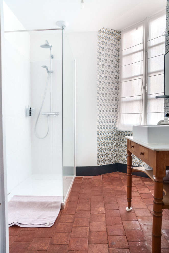 Foto på ett lantligt badrum med dusch, med en hörndusch, brun kakel, perrakottakakel, vita väggar, klinkergolv i terrakotta, ett konsol handfat och träbänkskiva