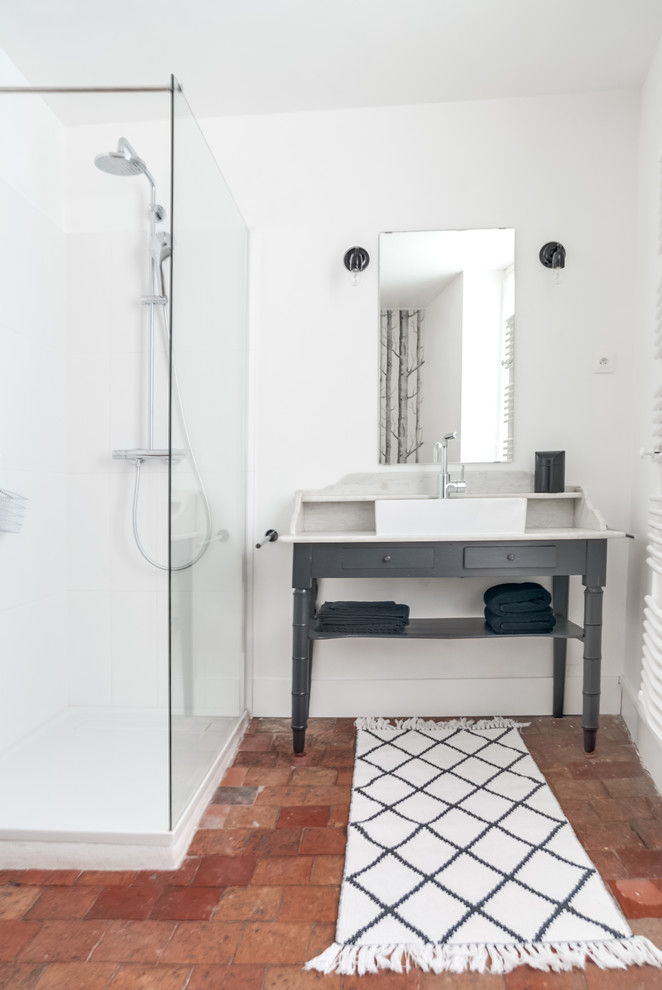 Cette photo montre une petite salle d'eau nature avec une douche d'angle, un carrelage marron, des carreaux en terre cuite, un mur blanc, tomettes au sol, un plan vasque et un plan de toilette en bois.