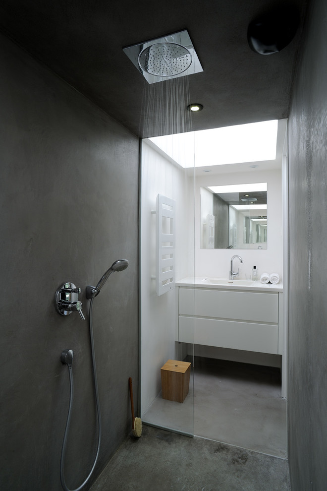 Skandinavisches Duschbad mit flächenbündigen Schrankfronten, weißen Schränken, bodengleicher Dusche, weißer Wandfarbe, Betonboden und integriertem Waschbecken in Lyon