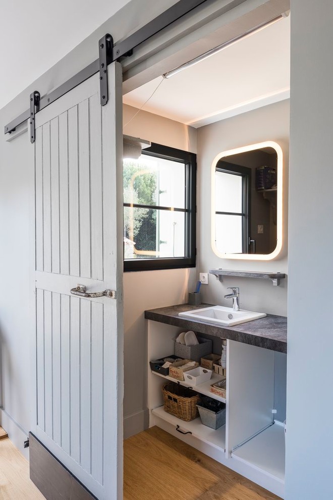 Imagen de cuarto de baño contemporáneo con armarios abiertos, puertas de armario blancas, paredes grises, suelo de madera en tonos medios, lavabo encastrado, suelo marrón y encimeras grises