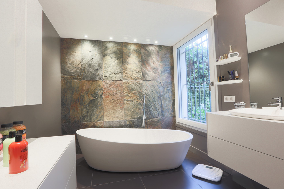 Источник вдохновения для домашнего уюта: главная ванная комната среднего размера в современном стиле с плоскими фасадами, белыми фасадами, отдельно стоящей ванной, серыми стенами, каменной плиткой и врезной раковиной