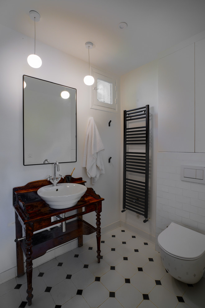 Lantlig inredning av ett mellanstort badrum med dusch, med luckor med profilerade fronter, vita skåp, en vägghängd toalettstol, vit kakel, perrakottakakel, vita väggar, klinkergolv i porslin, ett nedsänkt handfat, träbänkskiva, svart golv och med dusch som är öppen