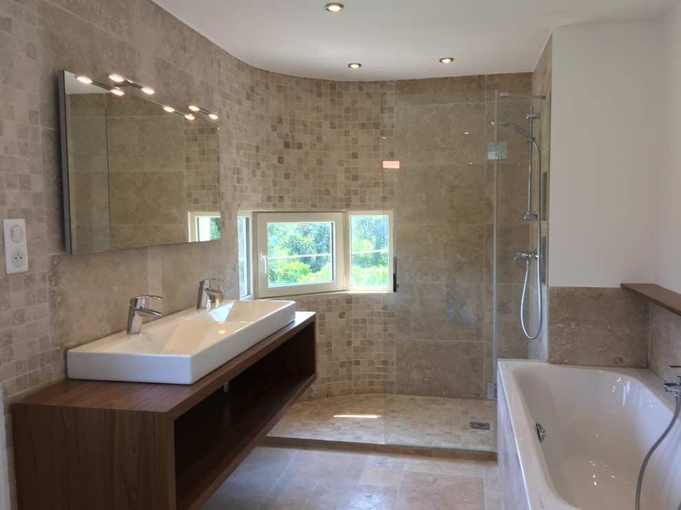 Cette image montre une salle d'eau méditerranéenne avec une douche à l'italienne, du carrelage en travertin, un sol en travertin, une grande vasque, un plan de toilette en bois et une cabine de douche à porte battante.