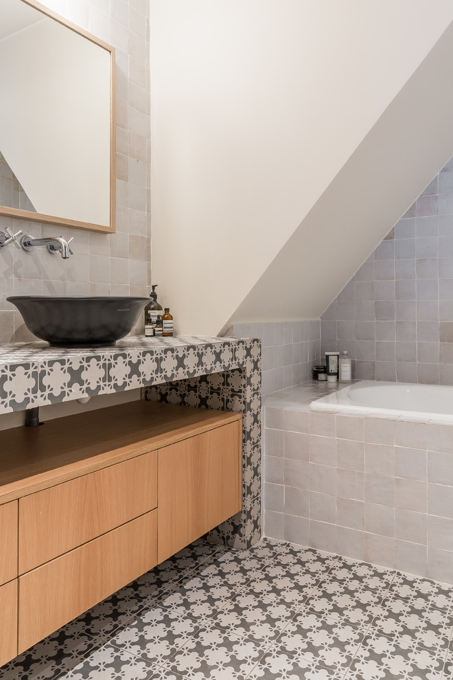 Photo of a mediterranean bathroom in Paris with flat-panel cabinets, medium wood cabinets, a built-in bath, white tiles, white walls, a vessel sink, tiled worktops, multi-coloured floors and multi-coloured worktops.
