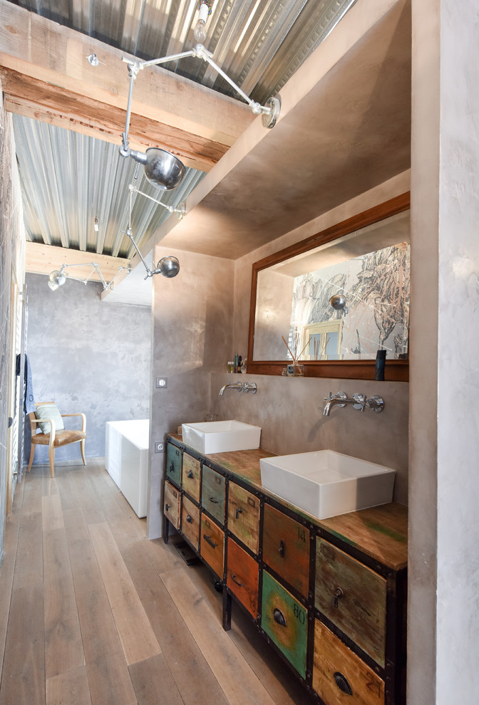 Cette photo montre une grande salle de bain principale éclectique en bois vieilli avec une vasque, un plan de toilette en bois, un mur gris, une baignoire indépendante et un placard à porte plane.