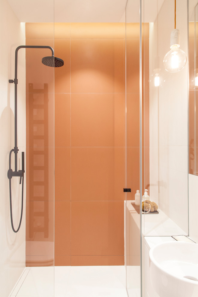 Skandinavisk inredning av ett mellanstort vit vitt badrum med dusch, med släta luckor, vita skåp, en öppen dusch, en vägghängd toalettstol, orange kakel, keramikplattor, vita väggar, cementgolv, ett fristående handfat, bänkskiva i akrylsten, flerfärgat golv och dusch med gångjärnsdörr