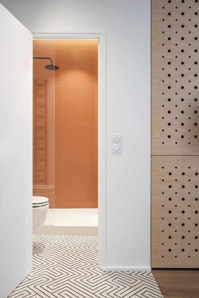 Exempel på ett mellanstort skandinaviskt vit vitt badrum med dusch, med släta luckor, vita skåp, en öppen dusch, en vägghängd toalettstol, orange kakel, keramikplattor, vita väggar, cementgolv, ett fristående handfat, bänkskiva i akrylsten, flerfärgat golv och med dusch som är öppen