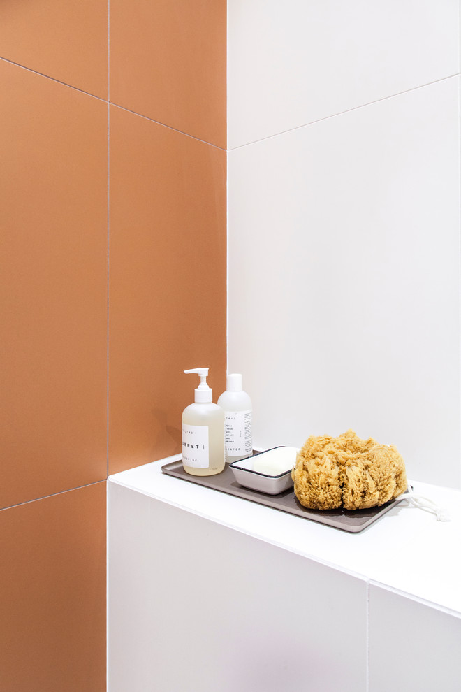 Exempel på ett mellanstort nordiskt vit vitt badrum med dusch, med släta luckor, vita skåp, en öppen dusch, en vägghängd toalettstol, orange kakel, keramikplattor, vita väggar, cementgolv, ett fristående handfat, bänkskiva i akrylsten, flerfärgat golv och dusch med gångjärnsdörr