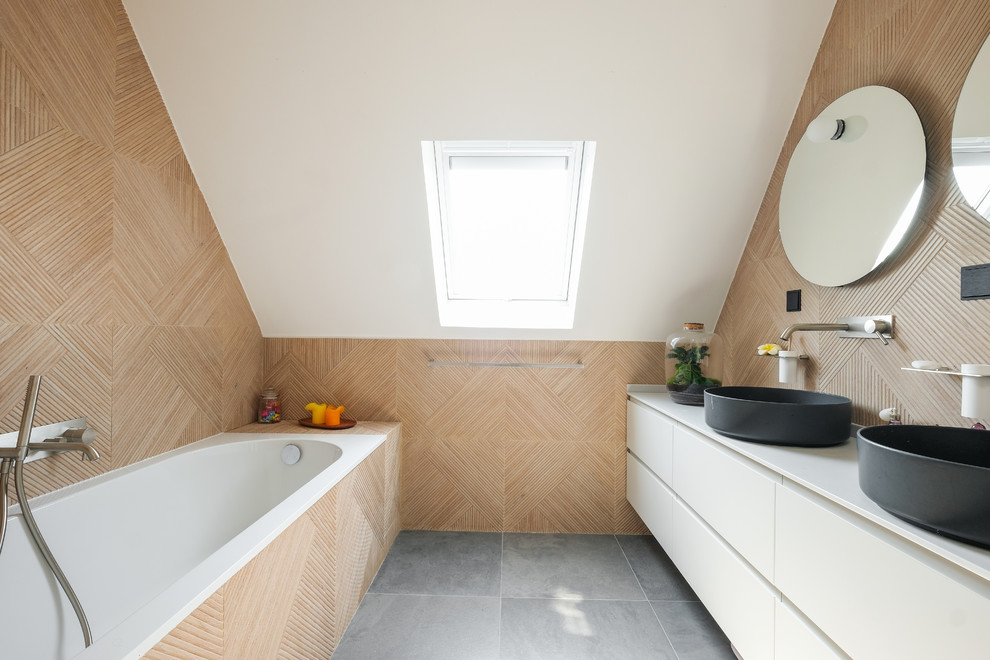 Cette image montre une salle d'eau design avec un placard à porte plane, des portes de placard blanches, une baignoire posée, une vasque, un sol gris et un plan de toilette blanc.