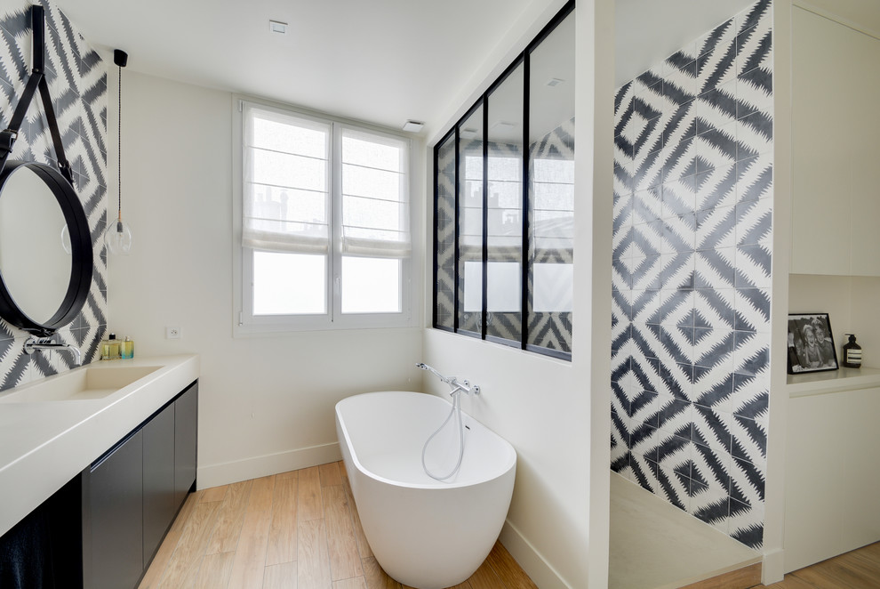 Modern inredning av ett badrum, med släta luckor, svarta skåp, ett fristående badkar, svart och vit kakel, flerfärgad kakel, vita väggar, ljust trägolv, ett integrerad handfat och med dusch som är öppen
