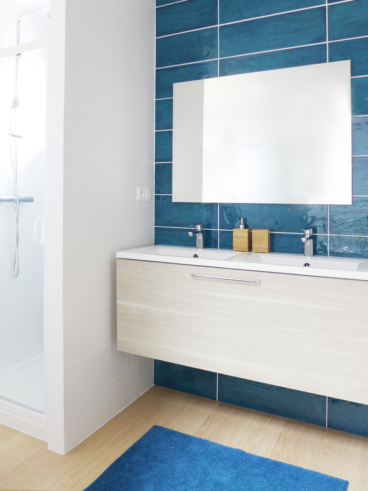 Cette image montre une salle de bain design en bois clair de taille moyenne avec un placard à porte plane, une douche d'angle, un carrelage bleu, un mur blanc, un plan vasque, un sol marron et une cabine de douche à porte battante.