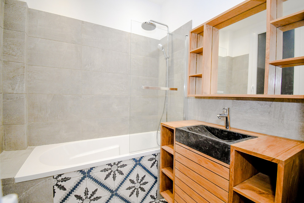 Tub/shower combo - mid-sized modern kids' gray tile and travertine tile ceramic tile and gray floor tub/shower combo idea in Marseille with an undermount tub, gray walls, an integrated sink, marble countertops and black countertops