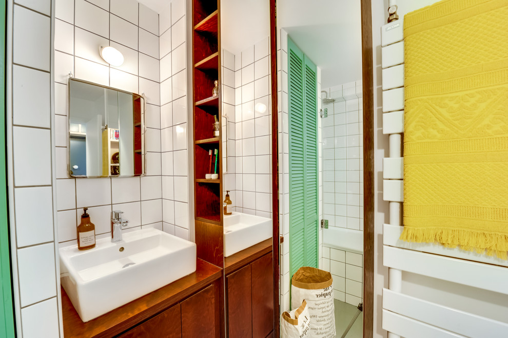 Cette photo montre une petite salle de bain principale rétro en bois foncé avec un carrelage blanc, des carreaux de céramique, un mur blanc, parquet peint, un plan de toilette en bois, un placard à porte plane, une baignoire encastrée et un lavabo posé.