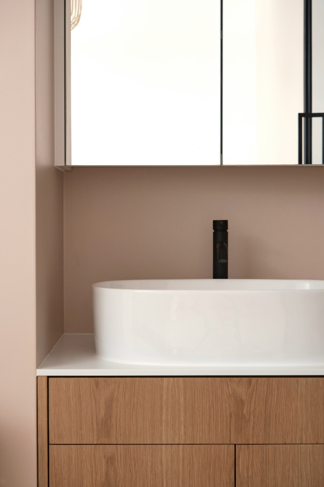 Idéer för att renovera ett litet funkis vit vitt badrum med dusch, med luckor med profilerade fronter, skåp i ljust trä, en dusch i en alkov, flerfärgad kakel, rosa väggar, ljust trägolv, ett konsol handfat, bänkskiva i akrylsten, brunt golv och dusch med gångjärnsdörr