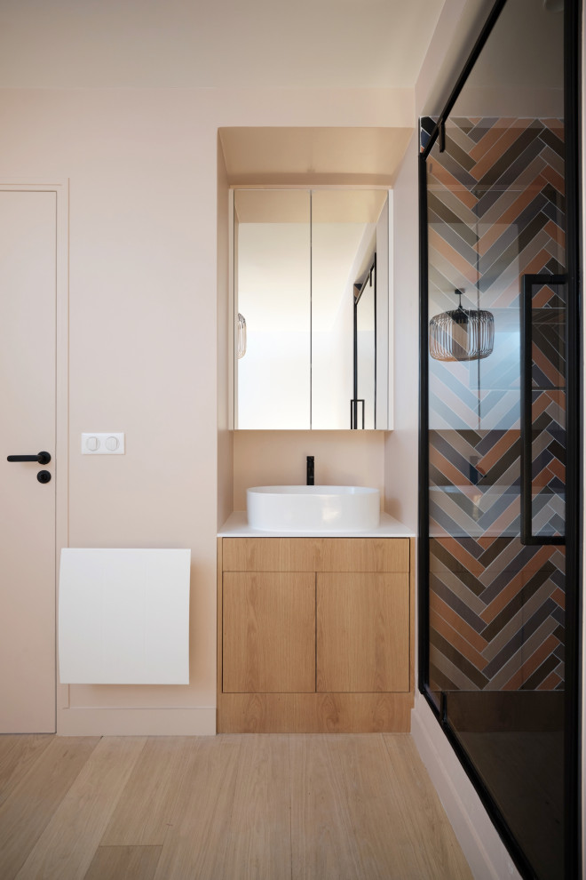 Inredning av ett modernt litet vit vitt badrum med dusch, med luckor med profilerade fronter, skåp i ljust trä, en dusch i en alkov, flerfärgad kakel, rosa väggar, ljust trägolv, ett konsol handfat, bänkskiva i akrylsten, brunt golv och dusch med gångjärnsdörr