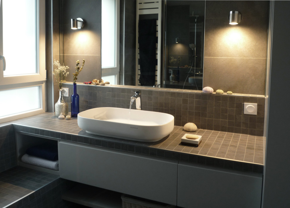Modern inredning av ett mellanstort en-suite badrum, med luckor med profilerade fronter, beige skåp, en kantlös dusch, en vägghängd toalettstol, grå kakel, mosaik, grå väggar, klinkergolv i keramik, ett avlångt handfat, kaklad bänkskiva, grått golv och med dusch som är öppen