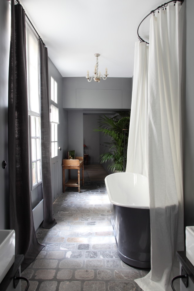 Cette photo montre une salle de bain principale éclectique de taille moyenne avec une baignoire indépendante, un mur gris, tomettes au sol et un lavabo posé.