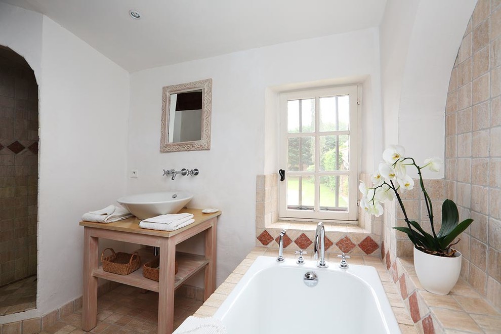 Cette image montre une douche en alcôve principale méditerranéenne en bois vieilli avec un placard sans porte, une baignoire posée, un carrelage beige, un mur blanc, une vasque, un plan de toilette en bois et un sol beige.