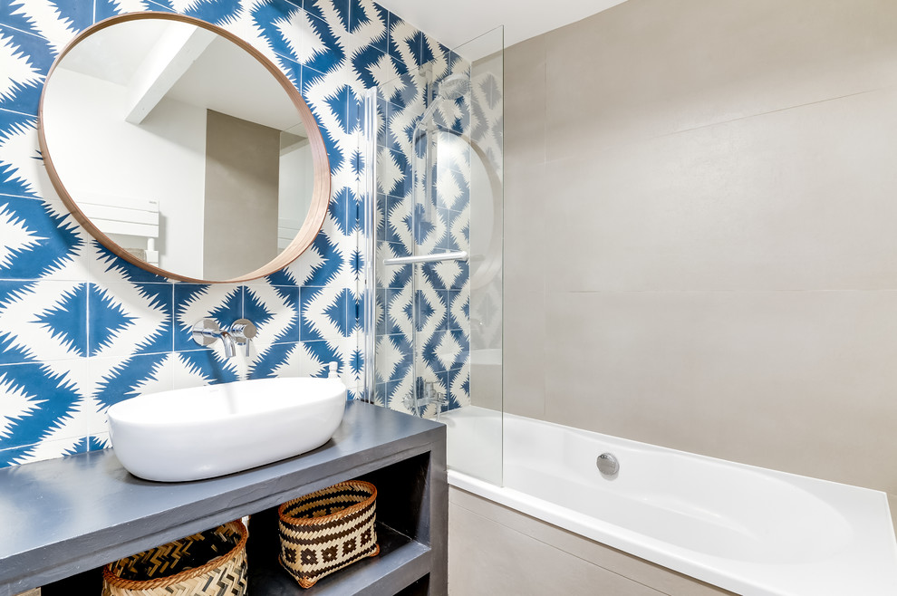Cette image montre une salle de bain principale design avec un placard sans porte, une baignoire encastrée, un carrelage bleu, des carreaux de béton, un mur gris, un lavabo posé et un plan de toilette en béton.