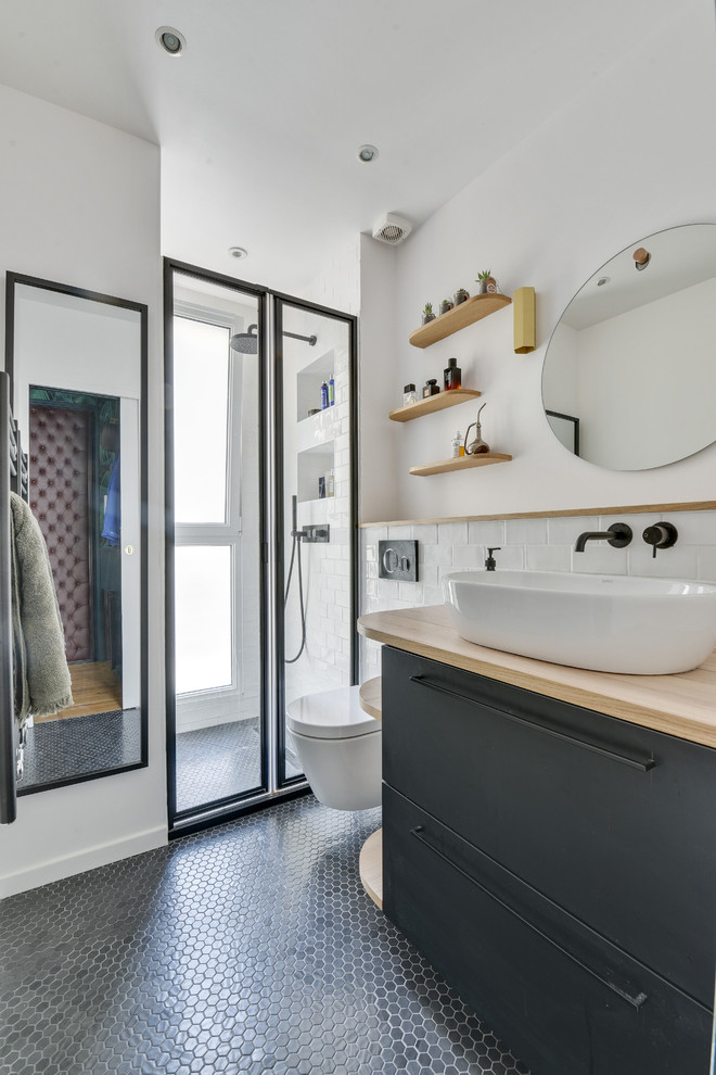 Inredning av ett modernt beige beige badrum med dusch, med släta luckor, svarta skåp, en dusch i en alkov, en vägghängd toalettstol, vit kakel, tunnelbanekakel, vita väggar, mosaikgolv, ett fristående handfat, träbänkskiva, svart golv och dusch med skjutdörr