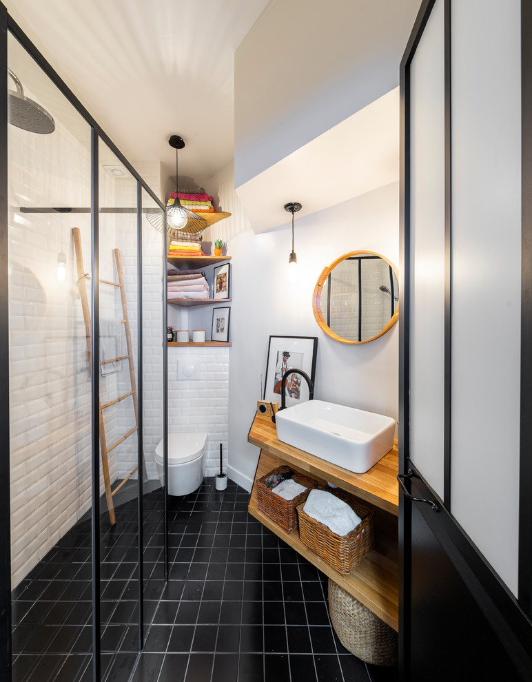 パリにあるお手頃価格の小さなコンテンポラリースタイルのおしゃれなバスルーム (浴槽なし) (バリアフリー、壁掛け式トイレ、サブウェイタイル、白い壁、セメントタイルの床、木製洗面台、黒い床、オープンシェルフ、中間色木目調キャビネット、白いタイル、ベッセル式洗面器、オープンシャワー、ベージュのカウンター) の写真