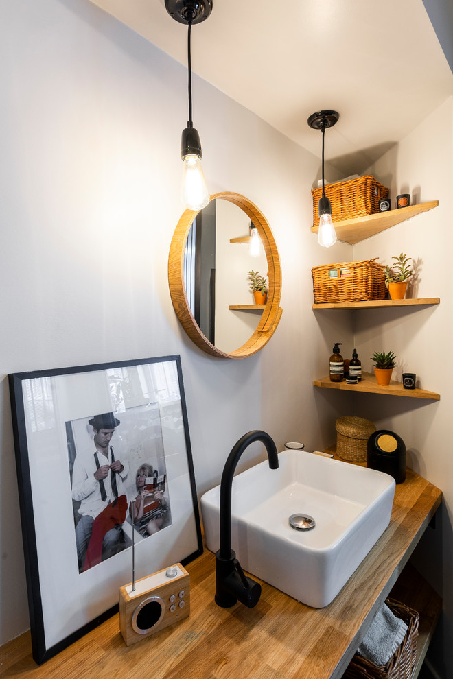 Inredning av ett modernt litet en-suite badrum, med en kantlös dusch, en vägghängd toalettstol, tunnelbanekakel, vita väggar, cementgolv, ett nedsänkt handfat, träbänkskiva och svart golv