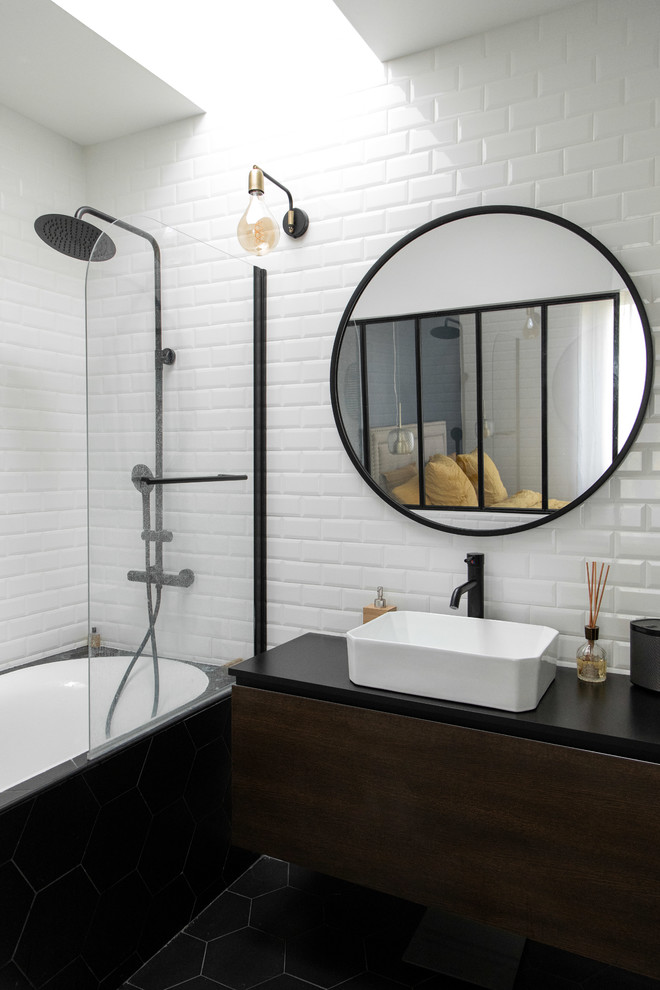 На фото: ванная комната в стиле лофт с плоскими фасадами, темными деревянными фасадами, ванной в нише, душем над ванной, белой плиткой, настольной раковиной, черным полом, открытым душем и черной столешницей
